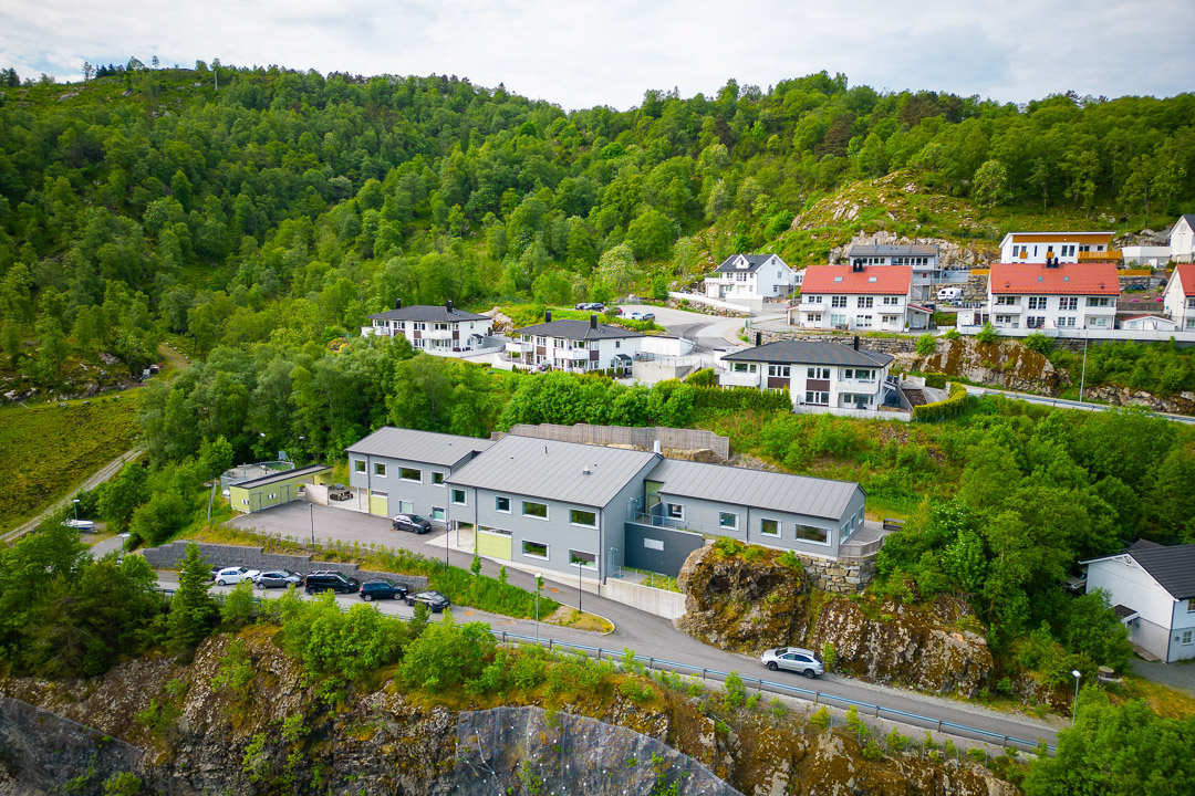 Dronebilde av Toppe med skog i bakgrunnen og parkering i front. 