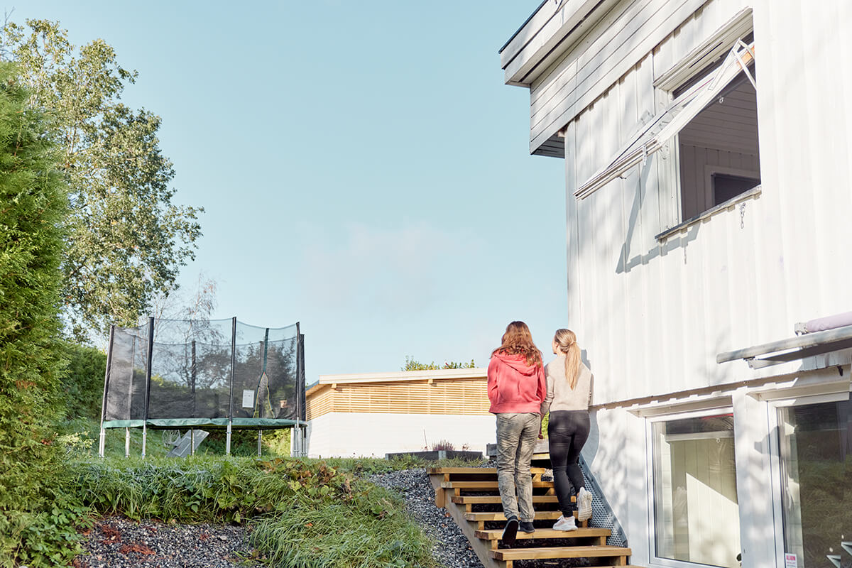 To kvinner går opp en trapp utenfor hovedhuset. Der er det en stor hage og trampoline