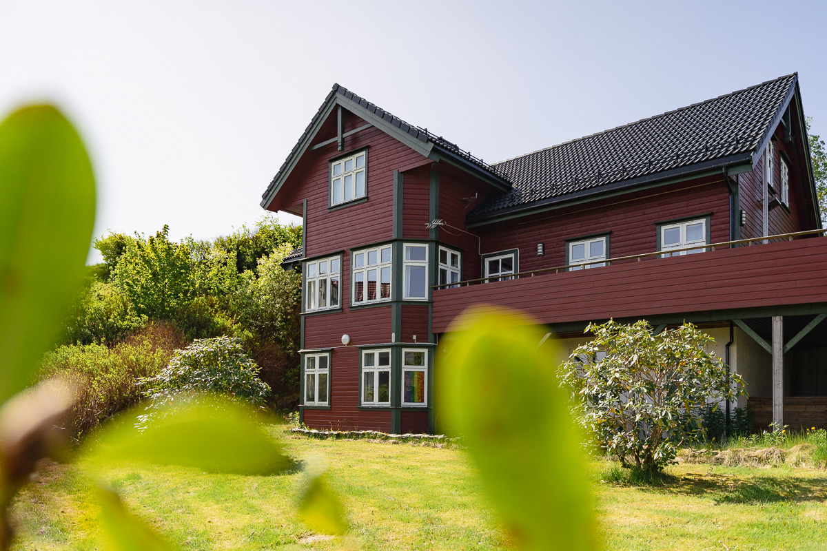 Huset på Sandsli, sett fra hagen. Grønn plen i front, stort brunt hus. 