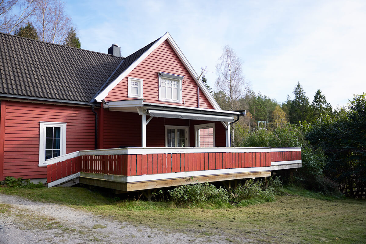 En rød enebolig med terrasse og hvitmalte vinduer