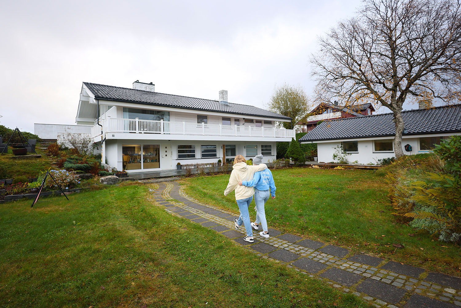 To ungdommer går sammen på en stenbelagt sti mot et hus. Foto.